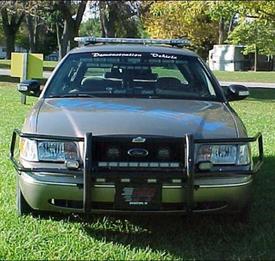A police car parked in the grass near some trees.