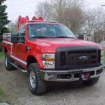 A red truck with two fire hoses strapped to the back of it.